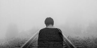 Man alone on train tracks photo by Gabriel / Unsplash, featured on Survivor Lit, a literary magazine for sexual assault survivors